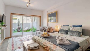 Een slaapkamer met een groot bed, een bank, een televisie en een glazen schuifdeur naar een buitenruimte met een stoel en tafel.