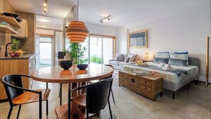 Een moderne woonkamer met een ronde houten tafel, zwarte stoelen, een bank en een bed met uitzicht op de omgeving.
