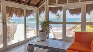 A room with large windows, a potted plant, a wooden table, and an orange sofa. - Orange Beach House 10bdr in Tulum Hotel Zone, Wake up every morning on the beach (Tulum)