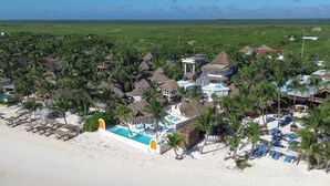 A resort with thatched-roof buildings, a swimming pool, and a beach area with sun loungers. - Orange Beach House 10bdr in Tulum Hotel Zone, Wake up every morning on the beach (Tulum)