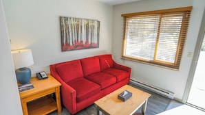A living room with a red sofa, a wooden coffee table, a lamp, and a painting on the wall. - Saddle Mountain Lodge (Blue River)