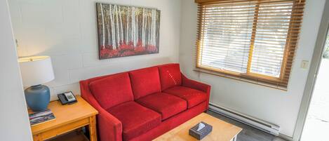 A living room with a red sofa, a wooden coffee table, a lamp, and a painting on the wall.