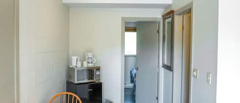 A narrow hallway with a wooden dining table and chairs, a microwave, and a refrigerator.