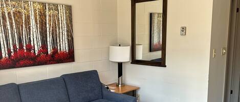 A room with a blue sofa, a wooden coffee table with a tissue box, a lamp, and a painting of trees.