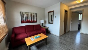 A living room with a red sofa, a wooden coffee table, a painting on the wall, a lamp, and a mirror. - Saddle Mountain Lodge (Blue River)