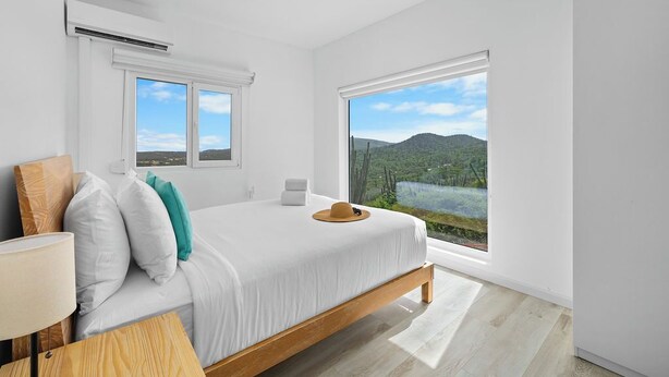 A modern bedroom with a large bed, two windows, and a view of a mountainous landscape. - 5BR @ Top of The Hill  Views Surrounded by Nature (Santa Cruz)