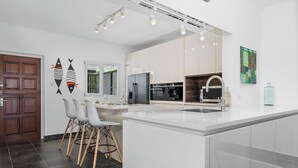 A modern kitchen with white cabinetry, a large island, and a dining area with chairs. - 5BR @ Top of The Hill  Views Surrounded by Nature (Santa Cruz)