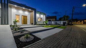 A modern building with a well-lit entrance, a paved driveway, and landscaped areas with plants.