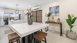 A modern kitchen with a marble countertop, wooden stools, and decorative plants.