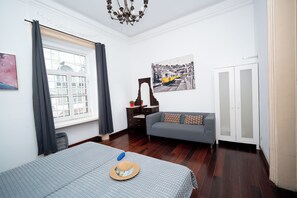 A room with a bed, a sofa, a window with curtains, a painting, and a cabinet.