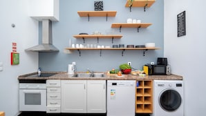 A compact kitchen with a microwave, sink, oven, and dishwasher. There are wooden shelves above the counter holding various kitchen items. - Palma Rooms Central Lisbon (Lisbon)