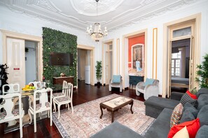 Un salón amplio con candelabro, televisor, zona de comedor con sillas y mesa, y sofá con cojines.
