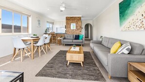 Ein modernes Wohnzimmer mit grauem Sofa, einem Holztisch und einem Essbereich mit weißen Stühlen und Holztisch.