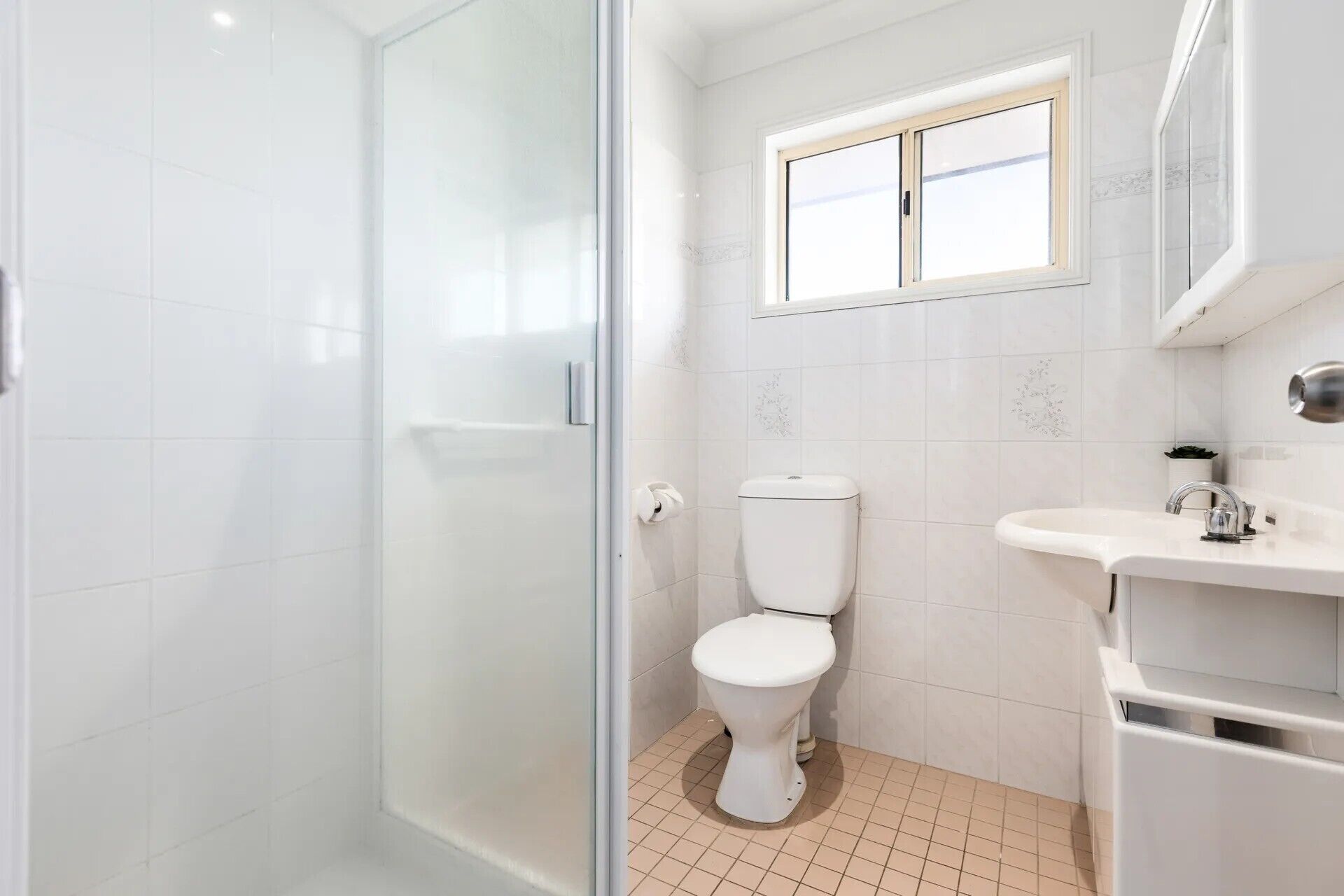 Un baño con inodoro, lavamanos y ventana sobre el inodoro.