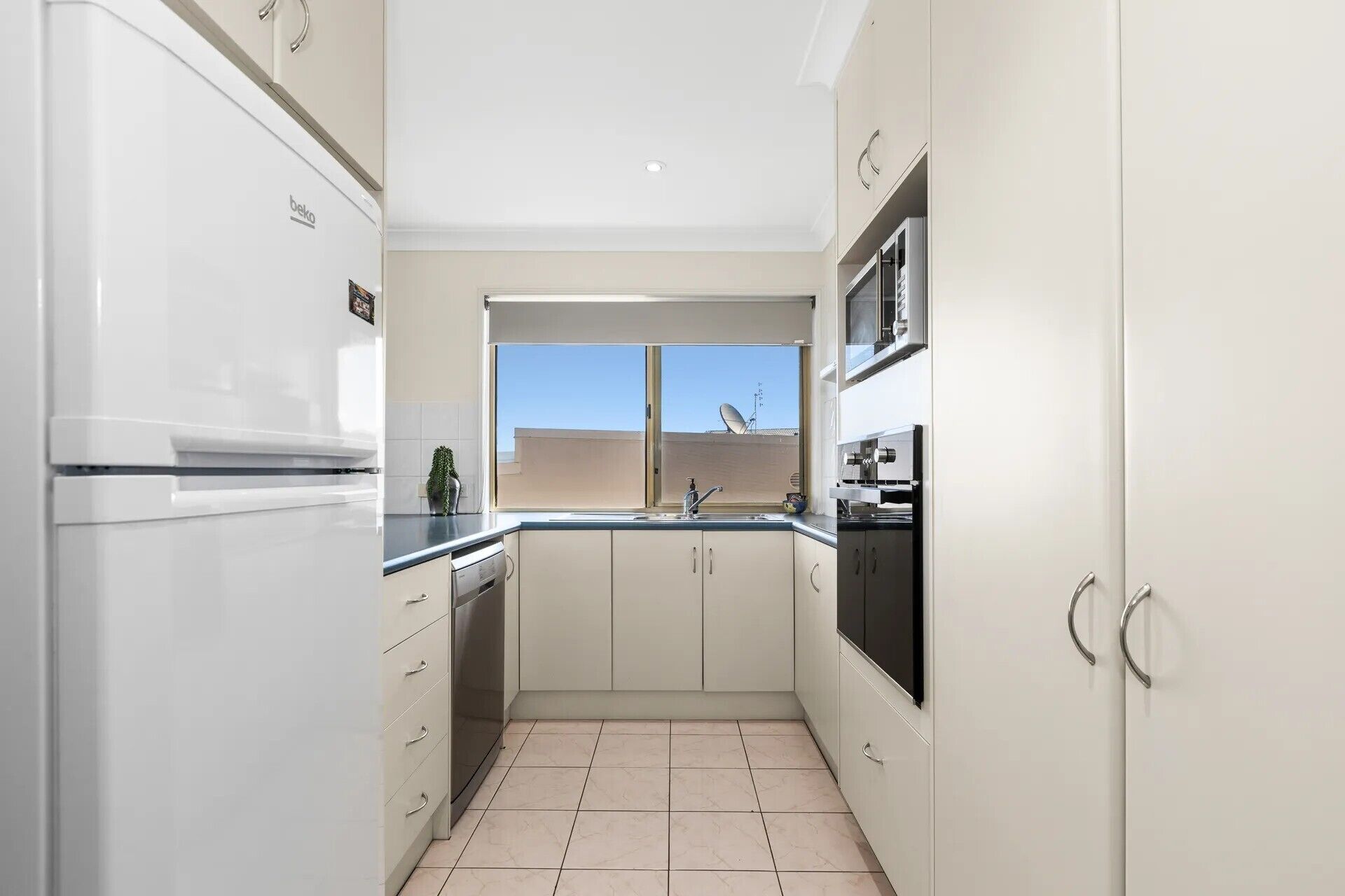 A modern kitchen with white cabinets, a built-in oven, and a window with a view of the sky.