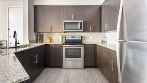 A modern kitchen with dark wood cabinets, stainless steel appliances, and a granite countertop. - Spacious 3BR | Pool, Gym, Near Beach and Speedway (Daytona Beach)