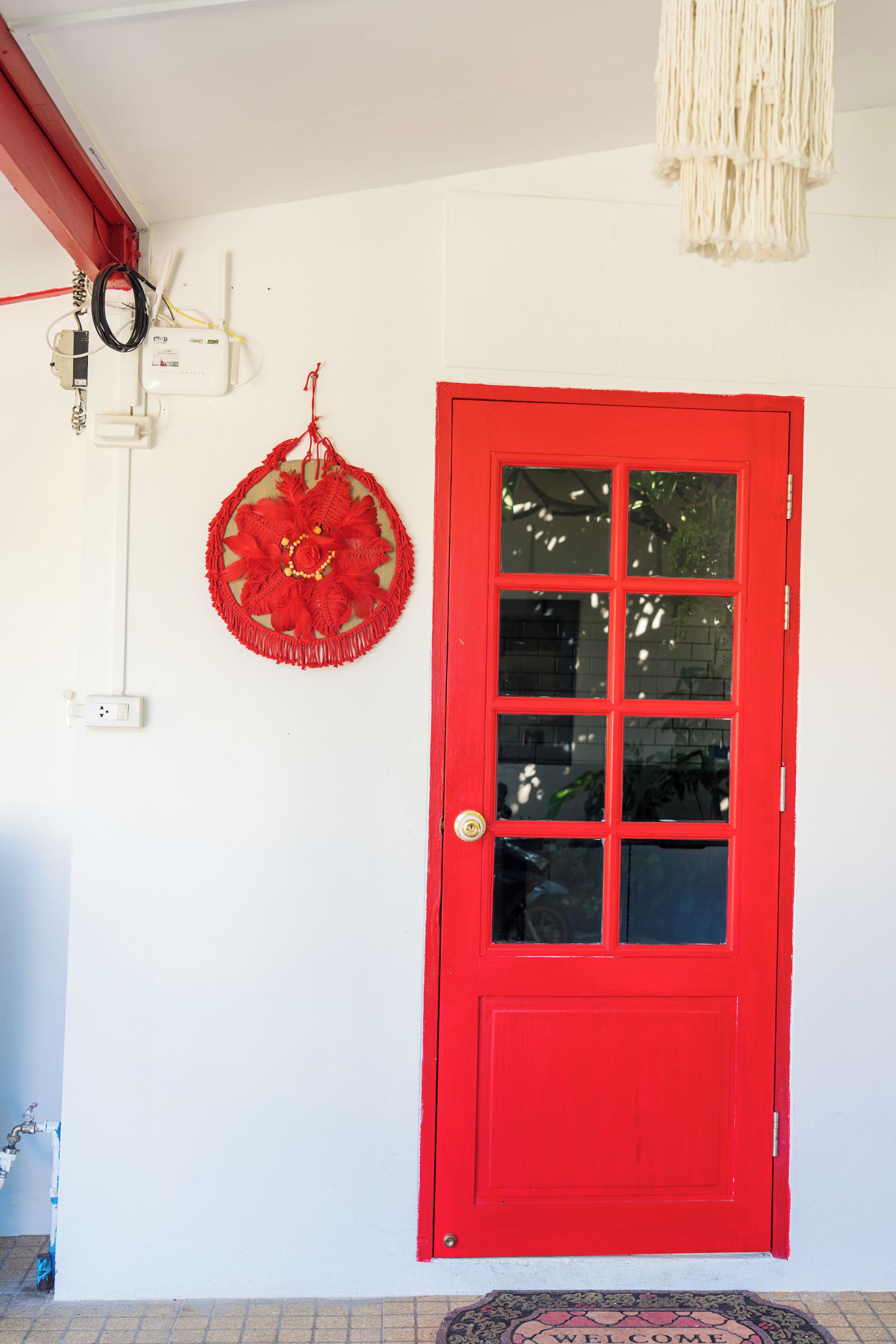 A red door with a glass panel, a wall-mounted electrical box, and a hanging decorative item.