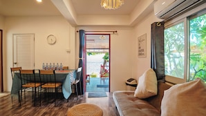 A living room with a sofa, a dining table with chairs, a clock on the wall, and a view of the outdoors through a window. - Oceanfront Villa at Bang Po Beach (Koh Samui)