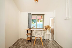 A room with a wooden desk, a white chair, a window with a view of the sea, and a small table with a vase. - Oceanfront Villa at Bang Po Beach (Koh Samui)