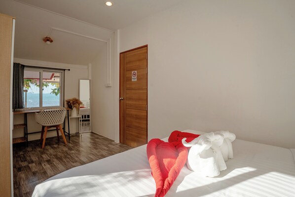 A hotel room with a bed, a desk, a chair, and a view of the sea.