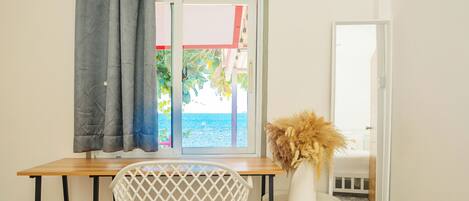 A room with a wooden desk, a white chair, a small white table with a vase, and a window with curtains.