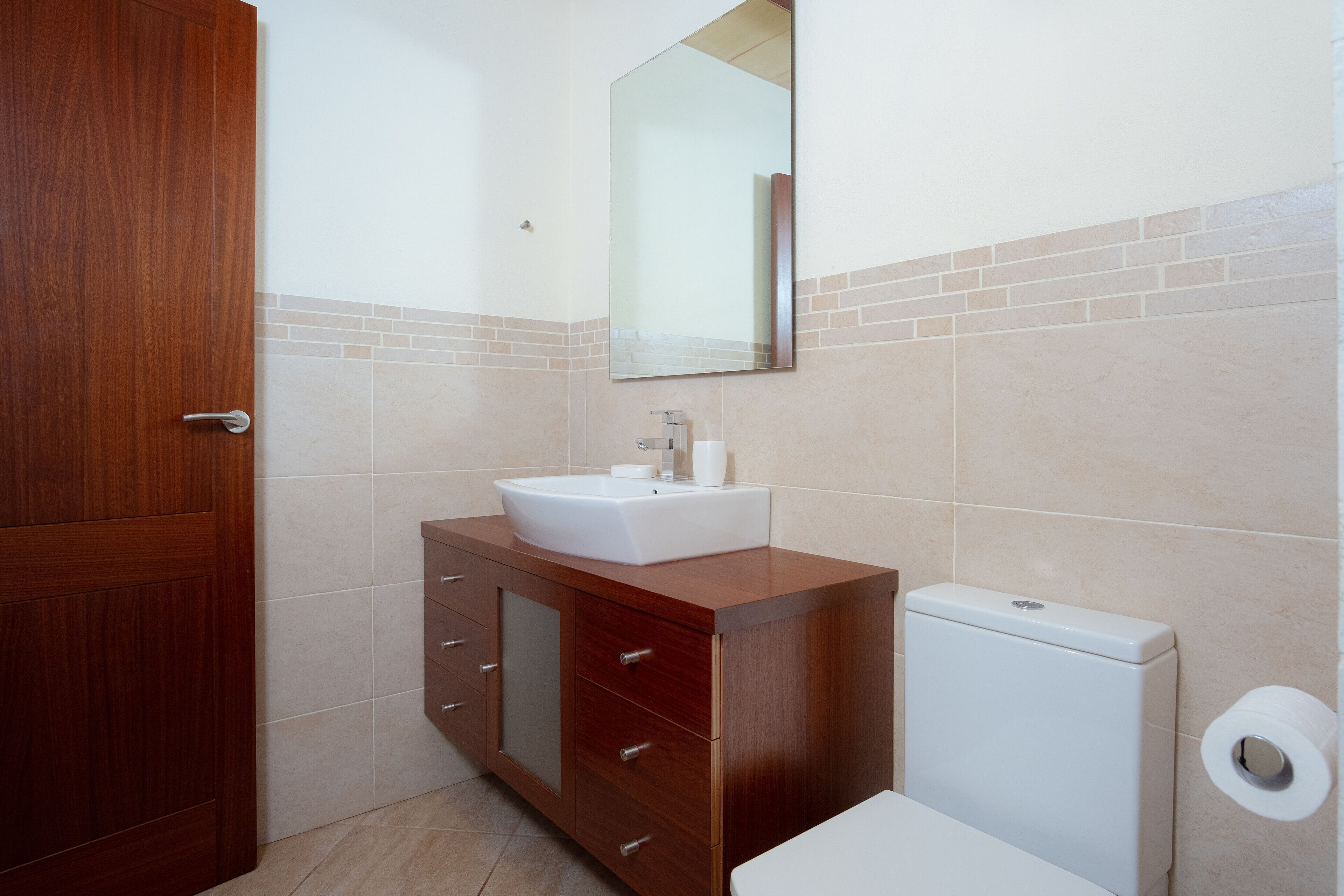 Een badkamer met een houten wastafelmeubel, een witte wastafel, een spiegel en een toilet.