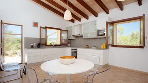 A modern kitchen with white cabinets, a round table, and clear chairs. - ES CLAPER - Beautiful estate with private pool and free Wi-Fi in Artà (Artà)