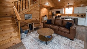 A wooden interior with a staircase, a brown leather sofa, a coffee table, and a kitchen area.