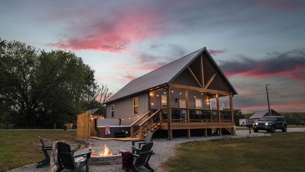 A large wooden cabin with a deck, outdoor seating, and a fire pit.