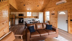 A cozy cabin interior with a leather sofa, wooden walls, a kitchen area, and a dining table.