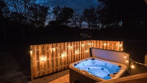 A hot tub in a wooden deck area with string lights.