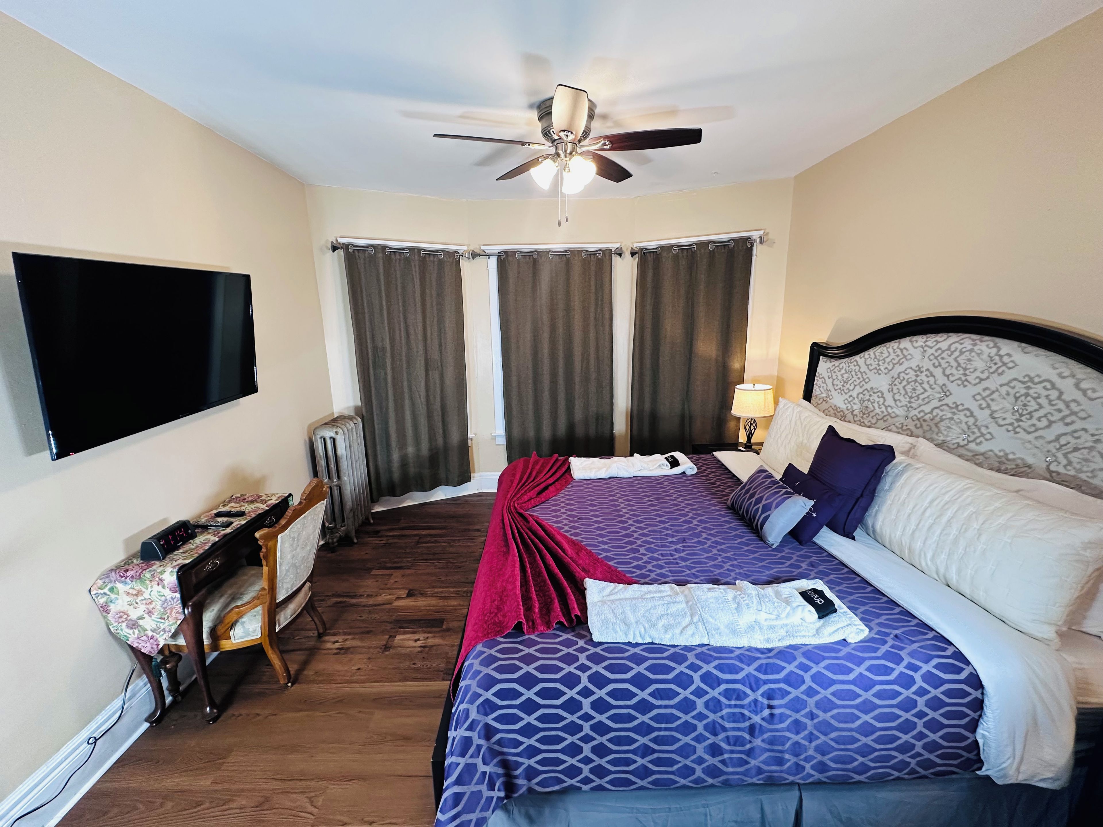 Une chambre d’hôtel équipée d’un lit, d’un ventilateur de plafond, d’une télévision, d’un radiateur, d’une table de chevet et d’une lampe.