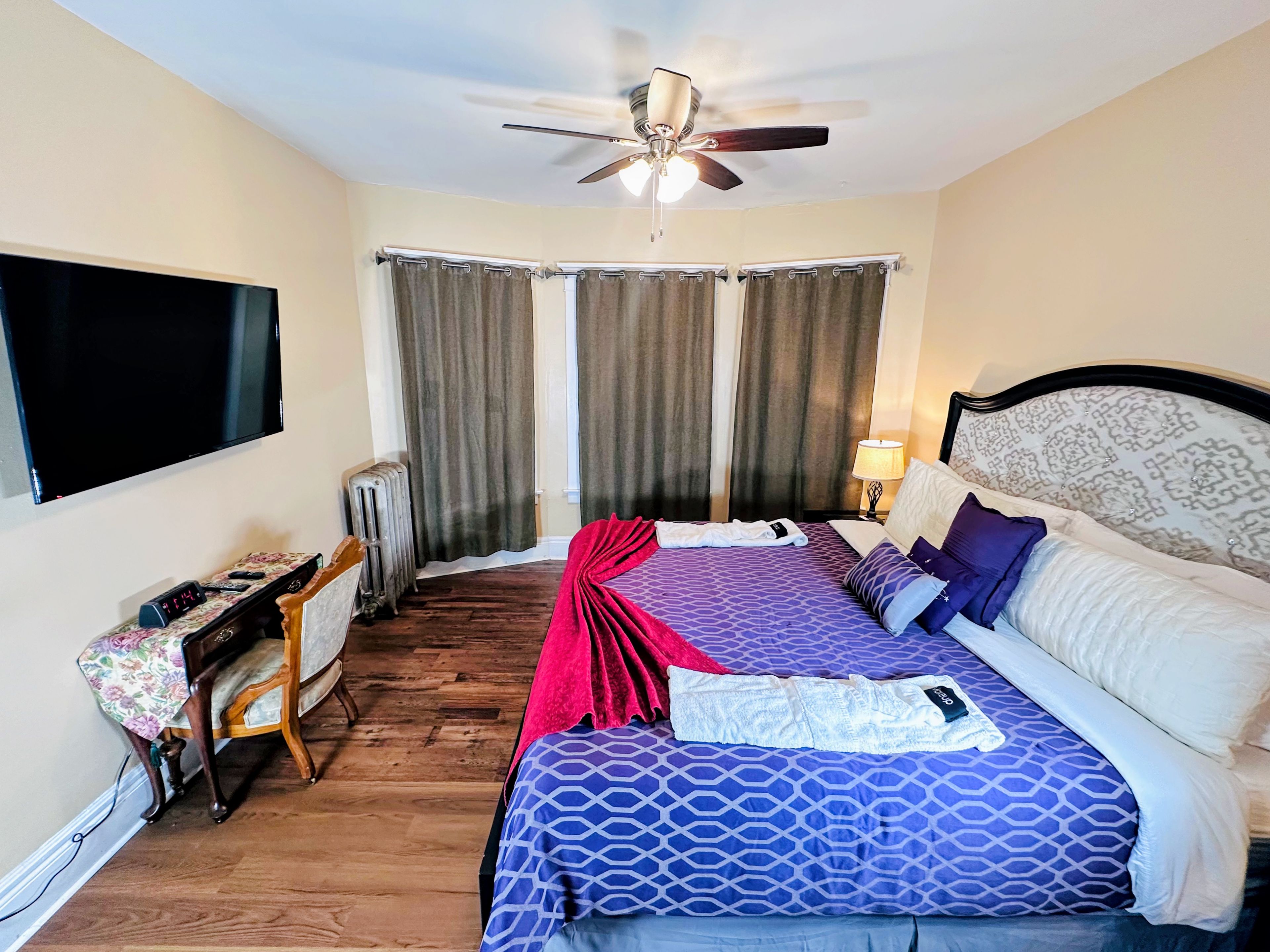 A hotel room with a bed, a ceiling fan, a TV, and a bedside table with a lamp.