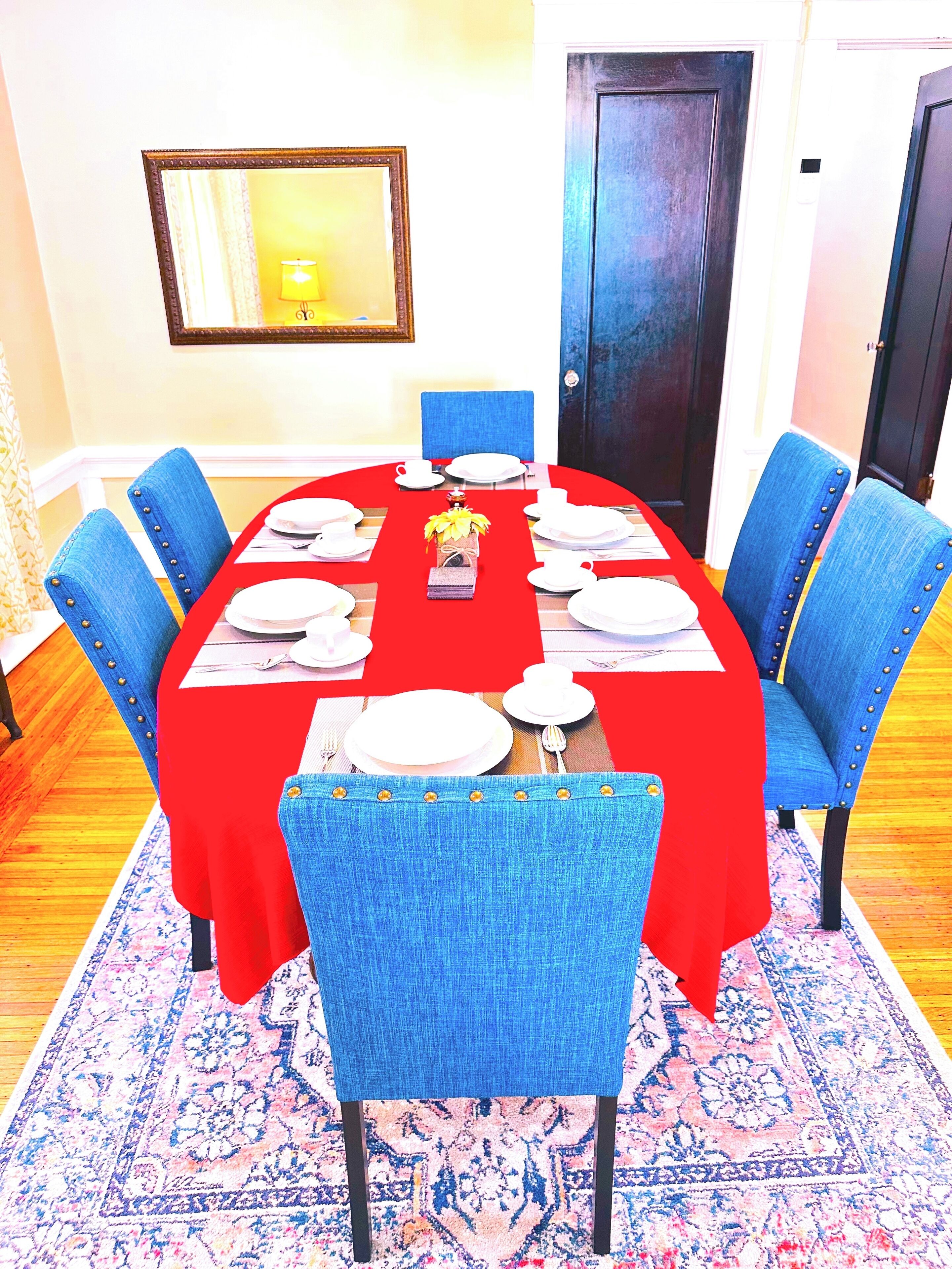 Un comedor con mantel rojo, sillas tapizadas en azul y una alfombra estampada.