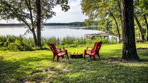 A lakeside setting with two red chairs facing a fire pit. - Cozy peaceful Lake Palestine Cabin Private dock, Kayak, fire pit Wifi (Chandler)
