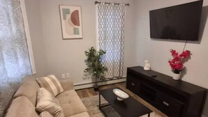 A living room with a beige sofa, a coffee table, a TV on the wall, a plant, and a small white statue.