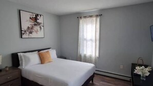 A bedroom with a bed, a nightstand, a dresser, a window with curtains, and a wall-mounted picture.