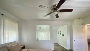 A bedroom with a bed, a ceiling fan, a window with blinds, and a hallway leading to a door. - Getaway by Lakes and Florida Southern, Fully Equipped House Near Top Attractions (Lakeland)