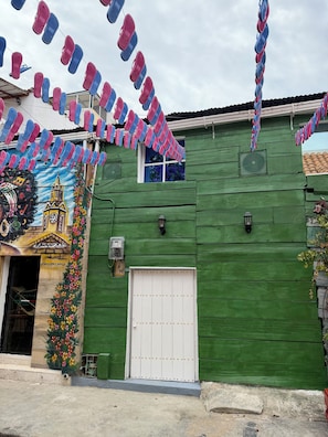A green building with a white door, a mural with a church, and a window.