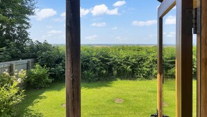 Een houten balkon met uitzicht op een weelderig groen veld en een heldere lucht.