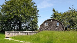 A rustic stone building with two windows, surrounded by lush green grass and trees. - Exmoor View Log Cabin, nr North Molton (South Molton)