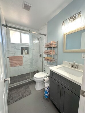 Une salle de bain avec une douche à parois de verre, des toilettes, un lavabo avec un miroir et des étagères avec des serviettes.