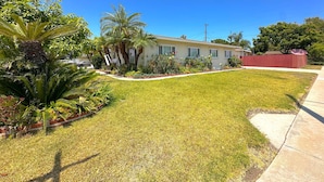 A residential house with a well-maintained lawn, palm trees, and a red fence. - Stay Near Disneyland – Clean, Spacious Anaheim Home for Families & Friends (Anaheim)