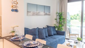 Ein modernes Wohnzimmer mit einem blauen Sofa, einem Esstisch gedeckt mit Tellern und Gläsern sowie einem Wandbild.