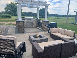 Un patio exterior con una parrilla, chimenea de piedra y mobiliario de mimbre.