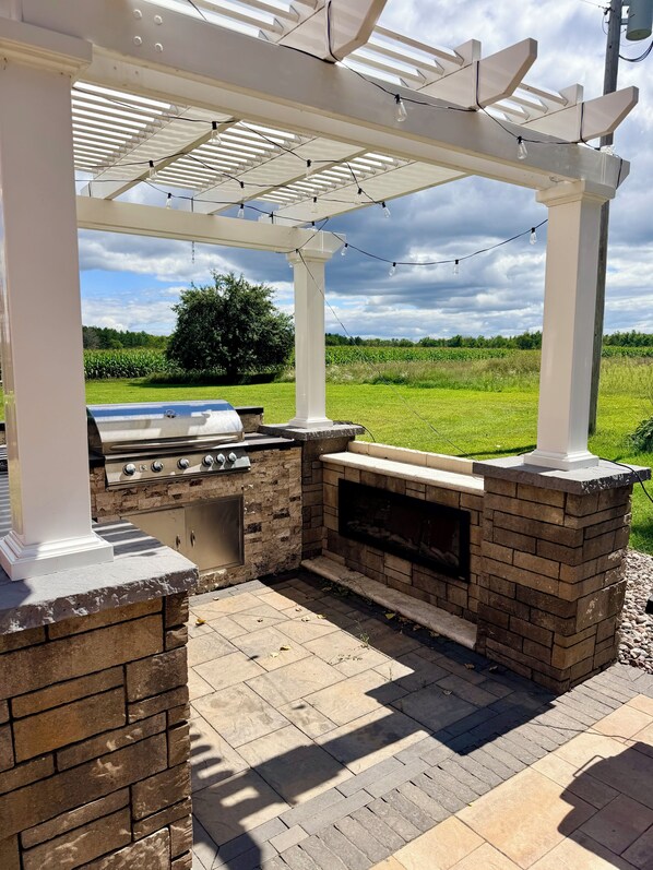 An outdoor kitchen with a grill and a built-in oven, under a pergola with string lights.
