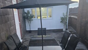 A patio area with a table and chairs, a black umbrella, and potted plants. - 2 Bed - Sleeps 6 - Private Balcony - City Centre (Wolverhampton)
