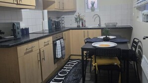A compact kitchen with wooden cabinets, a black countertop, a sink, and a dining area with a table and chairs. - 2 Bed - Sleeps 6 - Private Balcony - City Centre (Wolverhampton)