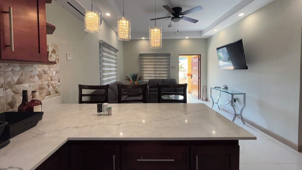 Una cocina moderna con una isla de mármol, luces colgantes, un ventilador de techo y un televisor de pantalla plana montado en la pared.