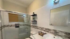 Un baño moderno con cabina de ducha de vidrio, lavamanos blanco y encimera de mármol.